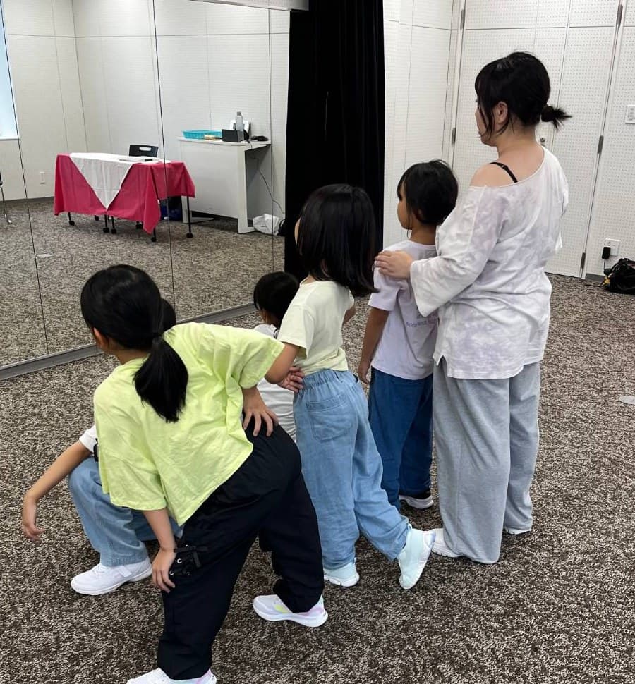 先生が子どもの肩に手を添えて、一緒に鏡を見ながら練習している様子